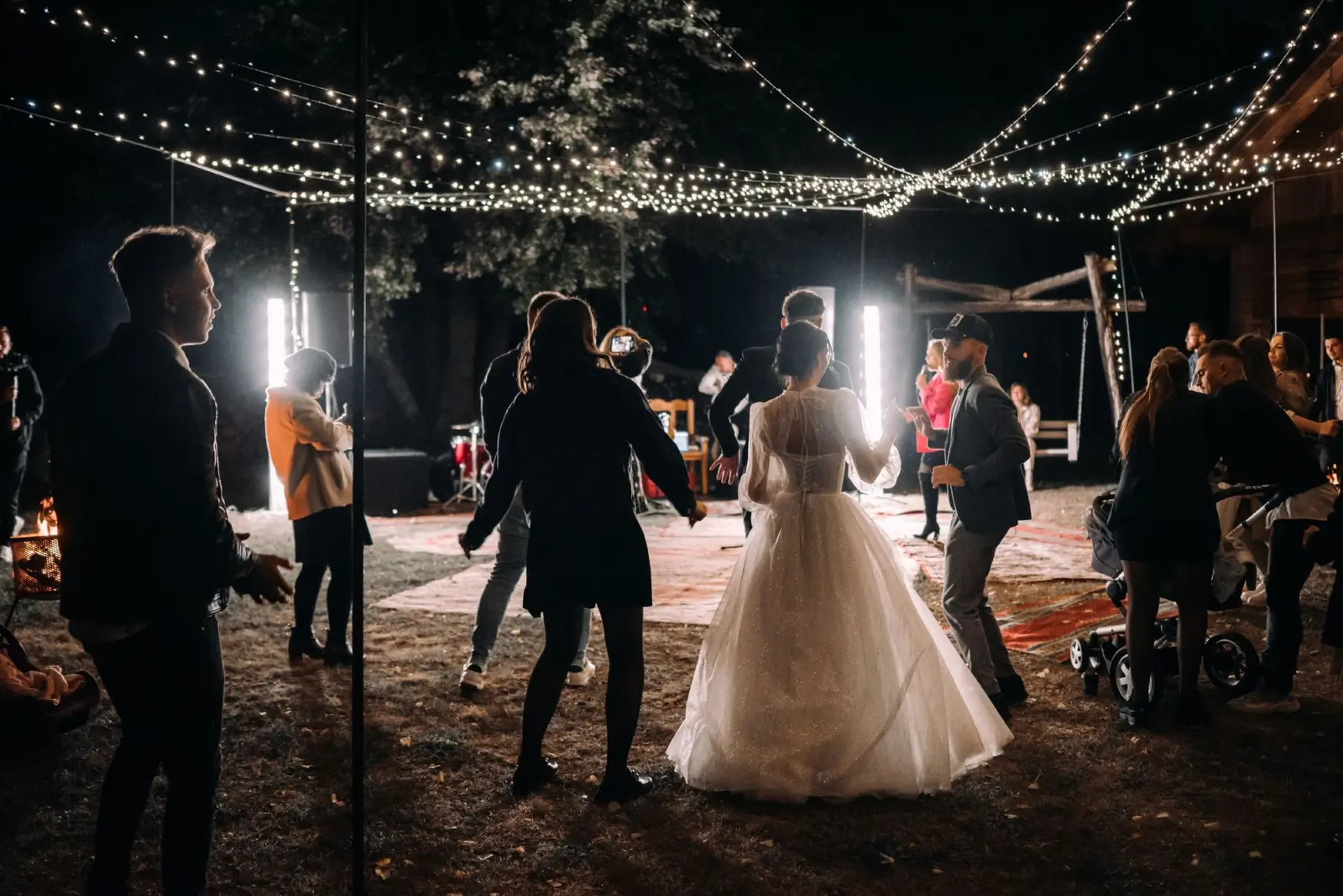 Bruidspaar en gasten dansen 's avonds onder lichtjes